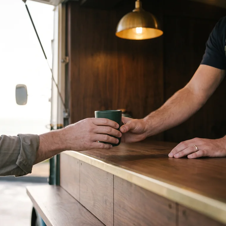 Deux mains se rejoignent au-dessus du comptoir au moment où une tasse en grès vert change de main.
