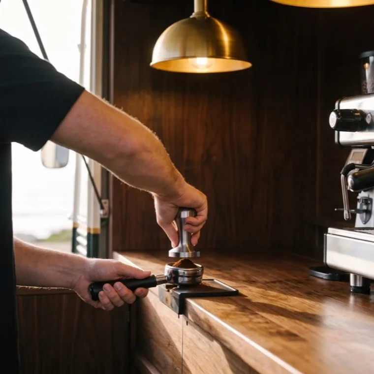 Les mains d’un barista tassent le café moulu dans un porte-filtre chromé.