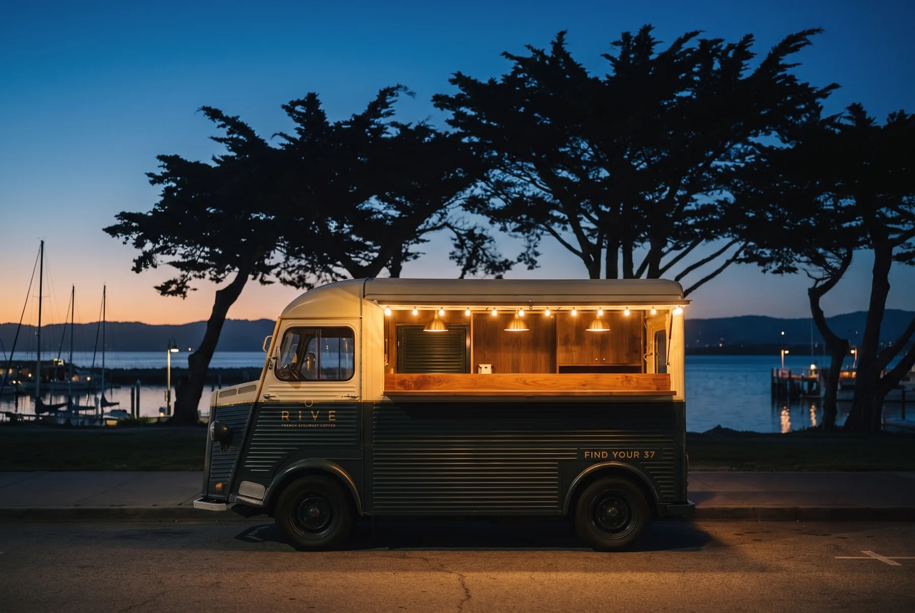 RIVE 37 ouvert à l’heure bleue sur le front de mer de Monterey, cyprès et mâts du port derrière, sa guirlande d’ampoules chaudes plus lumineuse que tout le reste.